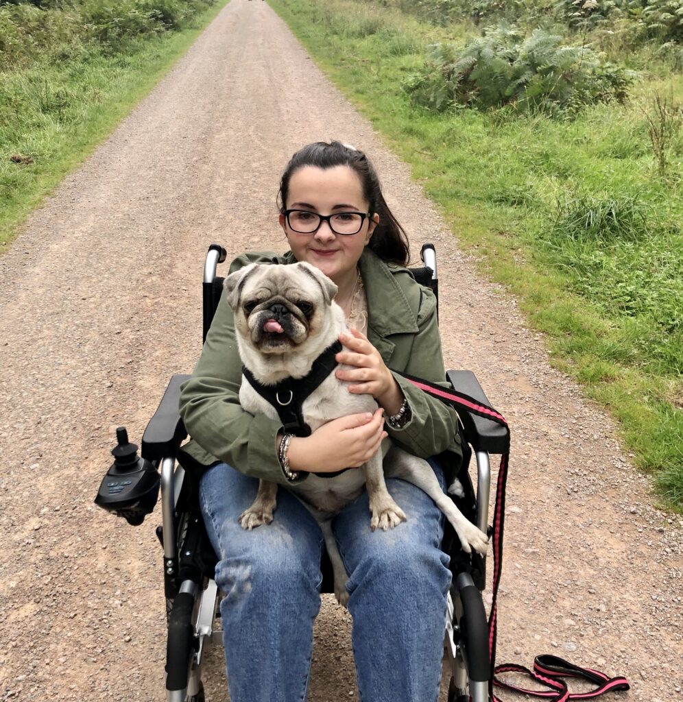 Tasmin sitting in a wheelchair with her dog (pug) in her lap. 

Tasmin lives with various rare conditions—APDS2 (activated phosphoinositide 3-kinase δ syndrome), postural orthostatic tachycardia syndrome, mast cell activation syndrome, oral allergy syndrome, histamine intolerance, aquaporin-4 antibody and MCADD (medium-chain acyl-CoA dehydrogenase deficiency). 