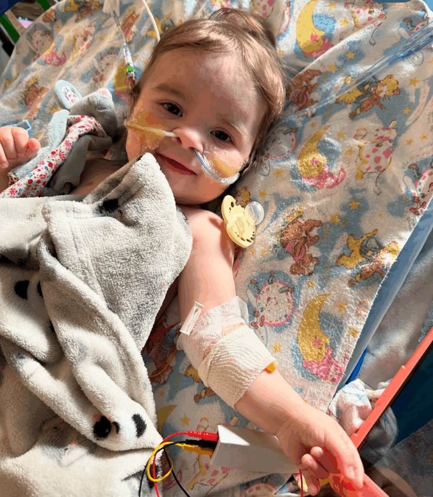 Mila in a hospital bed with an NG tube in either nostril. She is smiling