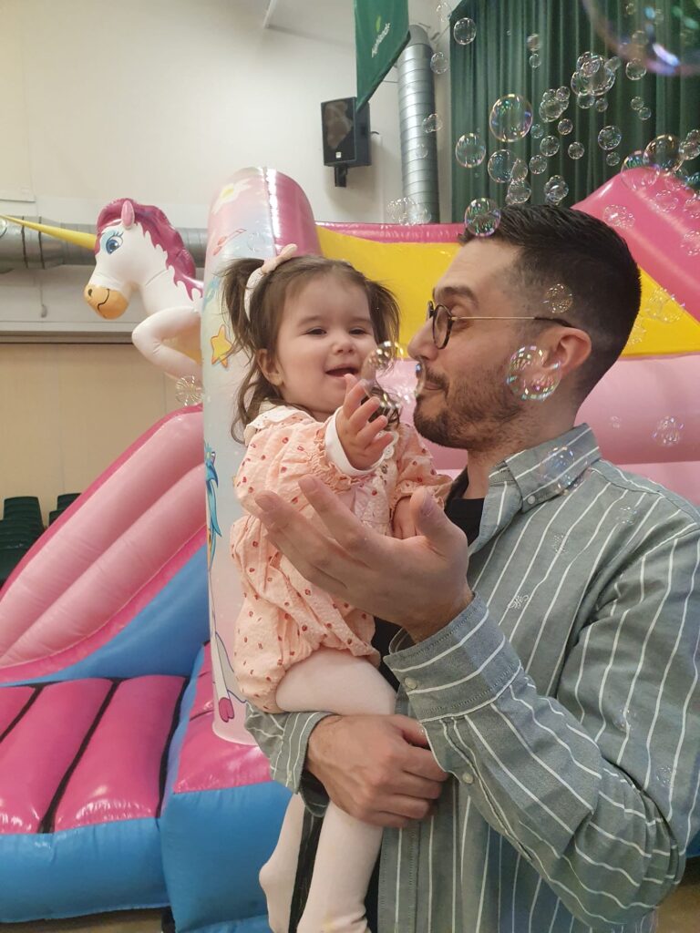 Mila with her dad Mete admiring bubbles. There is a bouncy castle in the background