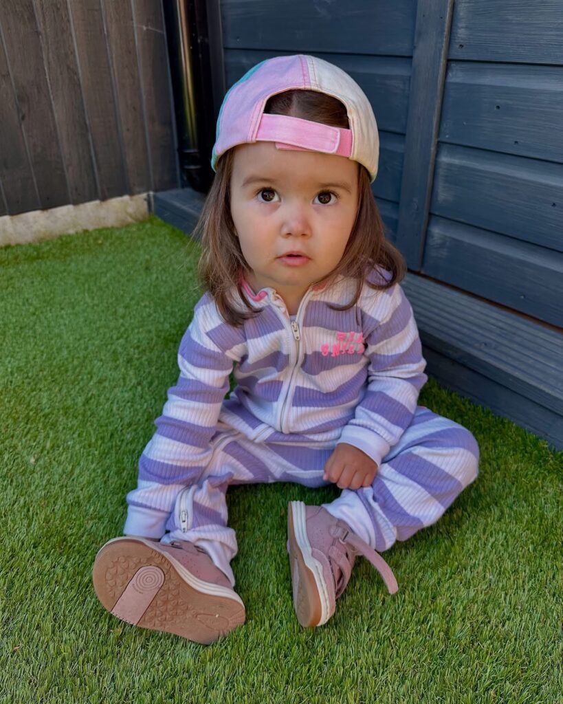 Mila sitting in grass with a backwards ballcap on