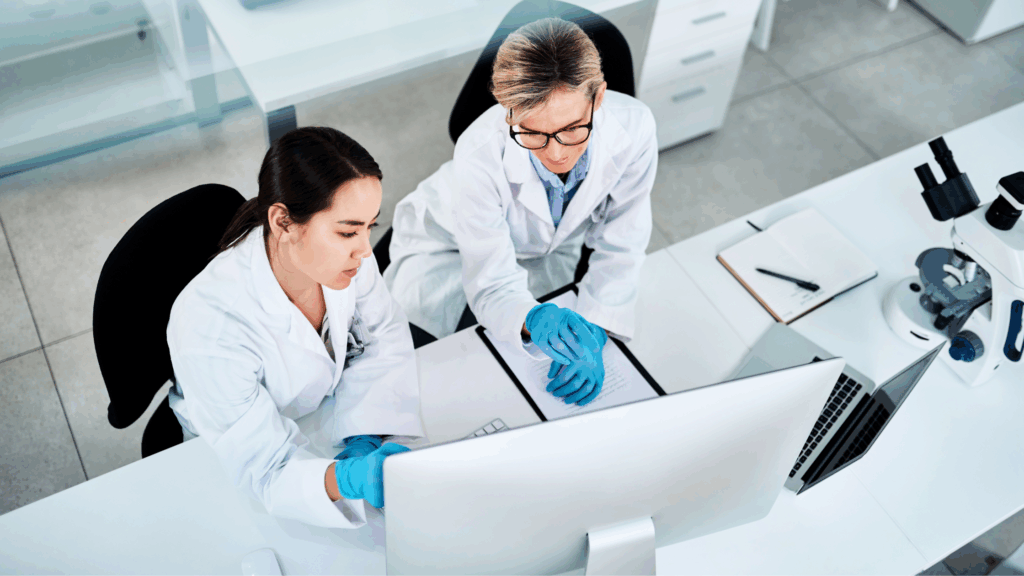 Image of two female scientists in white lab coats, looking at data on a computer in a lab