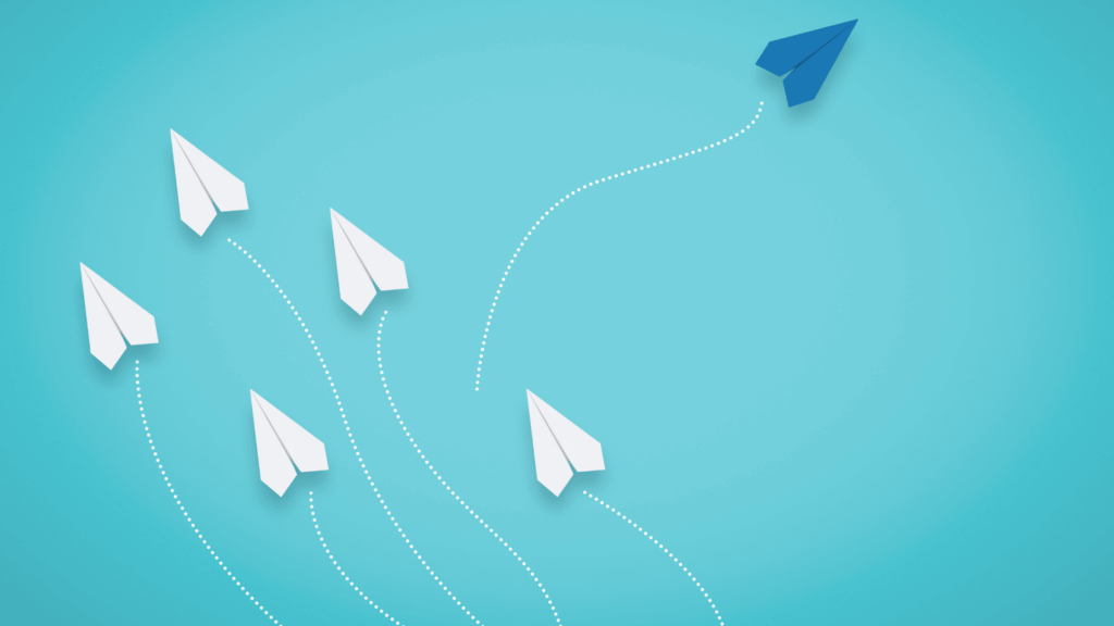 Image of 5 white paper planes heading in one direction and one blue paper plane forging a new path