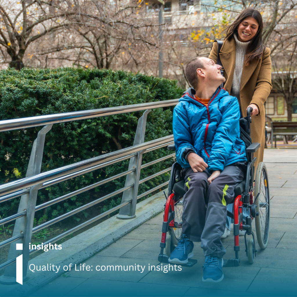 Image of a young man in a wheelchair looking back and laughing with the lady pushing him