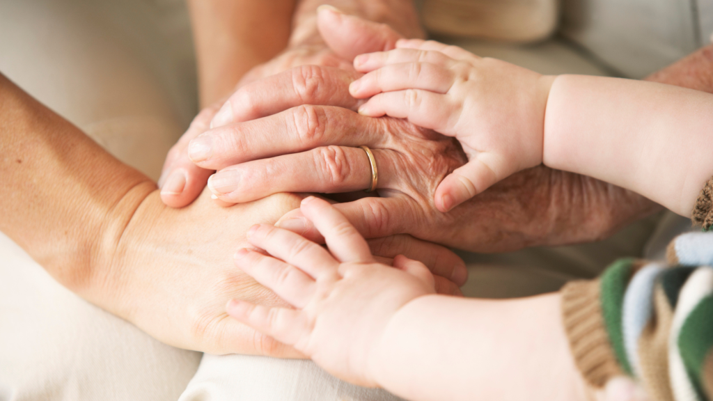 Photo of many hands holding, of different ages, representing multiple generations