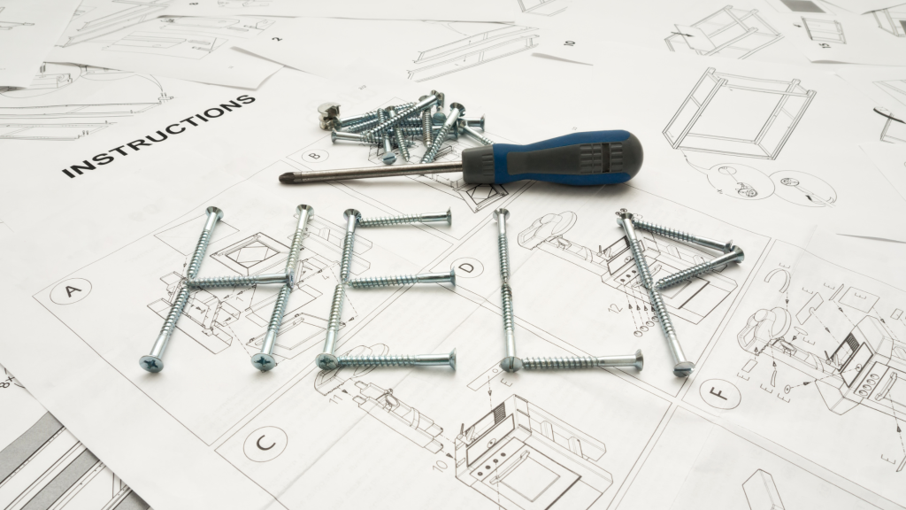Photo of some flat pack furniture instructions with a screwdriver on top and screws spelling out the word 'help'.