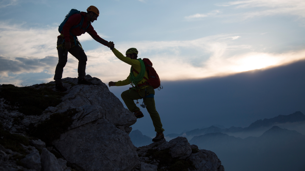Photo of someone reaching down to help someone else up a cliff, to denote trust and support.