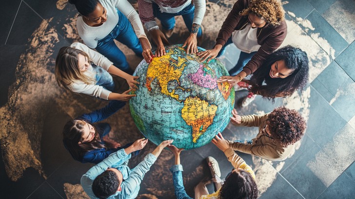 Image of multiple people touching a large globe signifying global collaboration